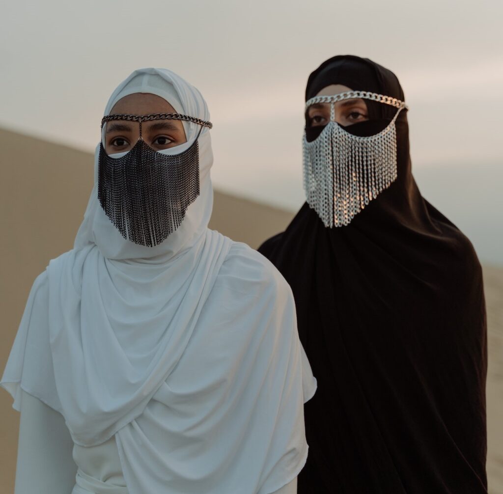 Two Muslim woman dressed in their traditional dresses and covering their faces standing in a desert area
