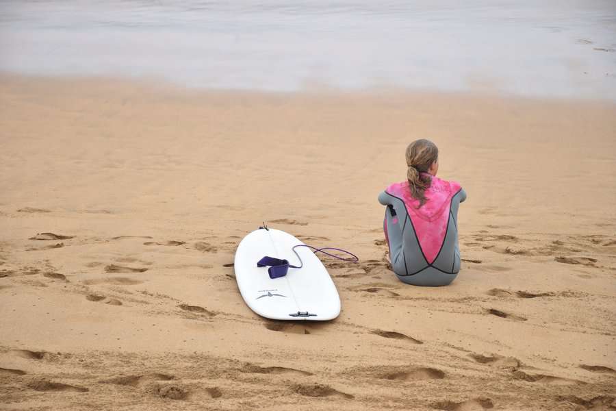 a woman sitting near the beach with her surfing board