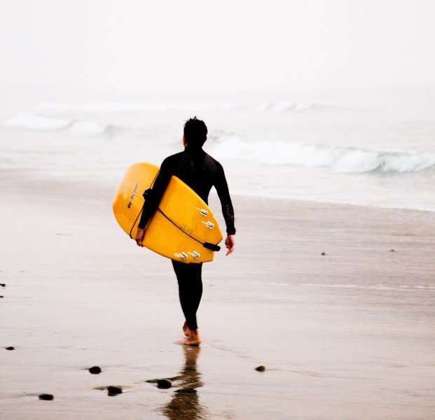 A man walking with his surfing board on the beach