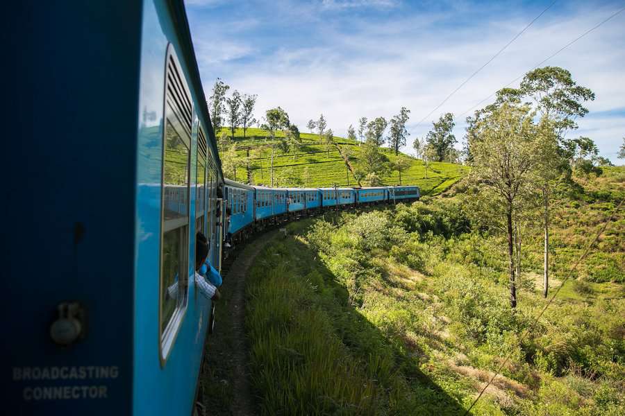 A blue colored train curving near the tea plantation hill