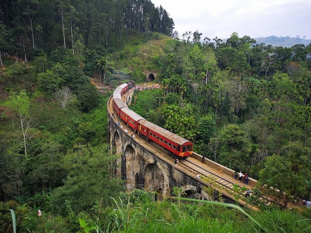 A red color train crossing the Ella bridge and tourists were taking pictures of it